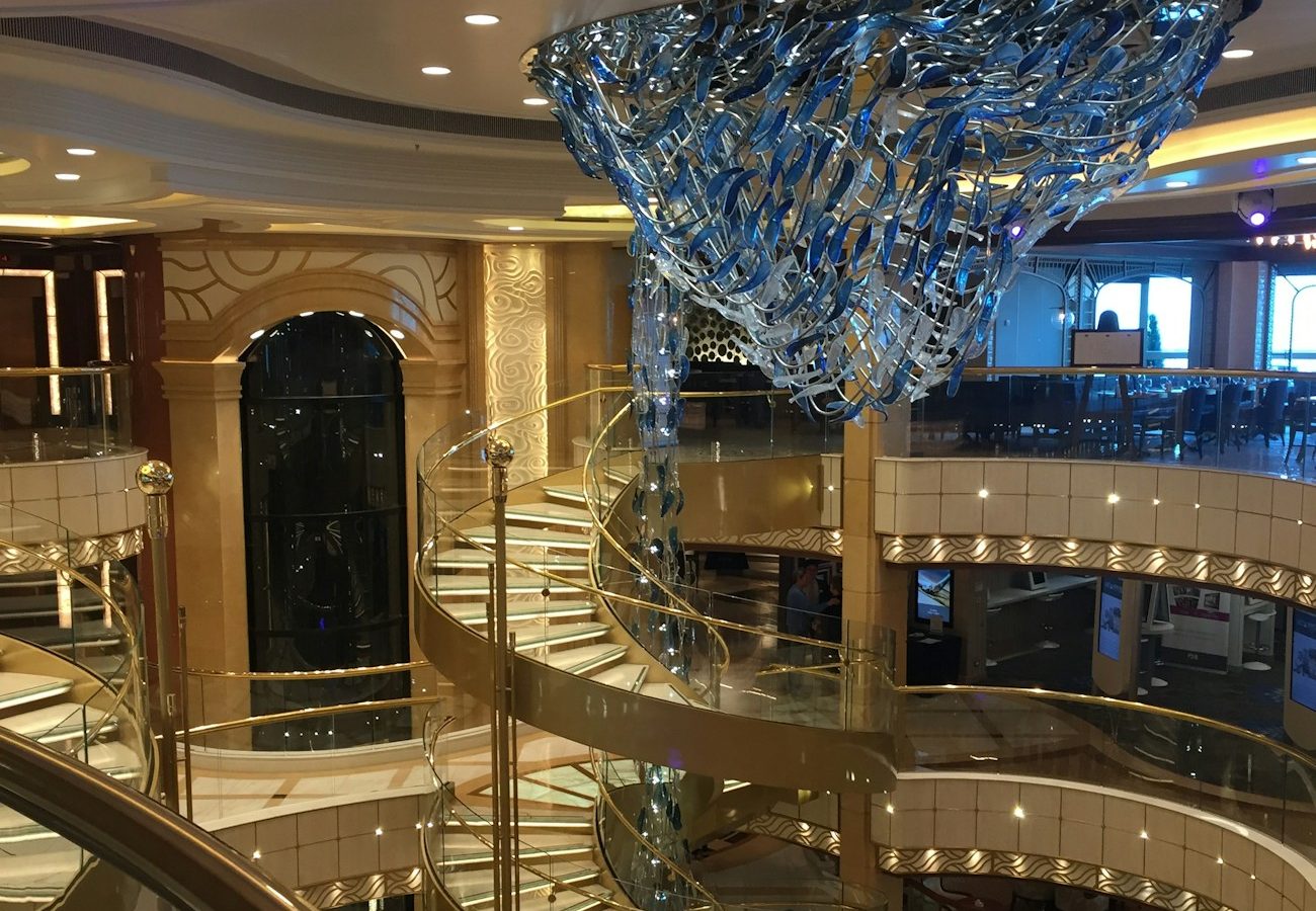 Opulent multi-deck cruise ship atrium with spiral staircase — the kind of suite-class ambience the MSC Yacht Club brochure sells at double fare